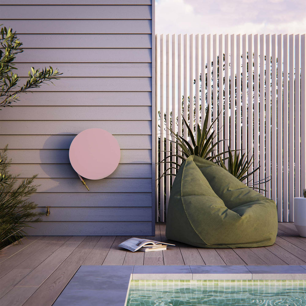 Freddy hose reel in pink, mounted on a poolside wall in a modern outdoor lounge setting with timber decking, a green bean bag, and a white slatted privacy screen. A functional and stylish garden accessory.
