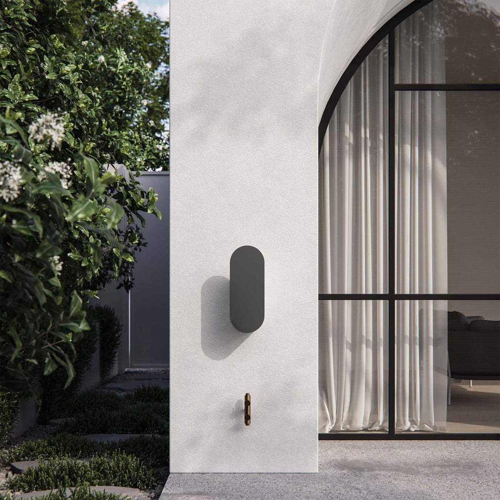 Martha hose reel in charcoal, mounted on an exterior wall of a modern home with arched windows and lush greenery. A minimalist outdoor storage solution for stylish spaces.