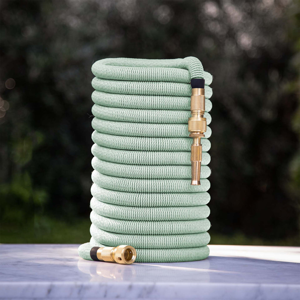 Fritz Tango Soft Expandable Garden Hose in green, coiled neatly on a marble surface, featuring durable brass fittings. Lightweight and kink-free design for effortless watering.