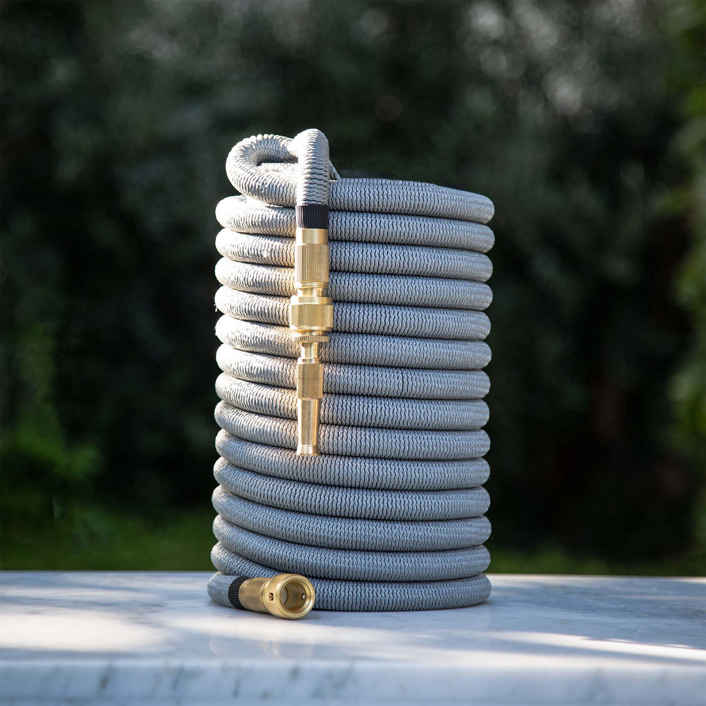 Fritz Tango Soft Expandable Garden Hose in light grey, neatly coiled on a marble surface, featuring solid brass fittings. Durable, lightweight, and kink-free for seamless gardening.