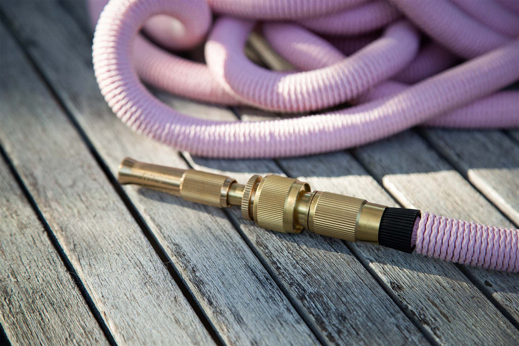 Close-up of the Fritz Tango Soft Expandable Garden Hose in pink, showcasing its durable brass nozzle and flexible design, resting on a chic wooden deck. Perfect for stylish and reliable garden watering.